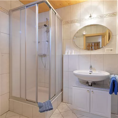 Ein modernes Badezimmer mit einer Duschkabine und einem Waschbecken. Blaue Handtücher und dekorative Elemente verleihen dem Raum eine einladende Atmosphäre.