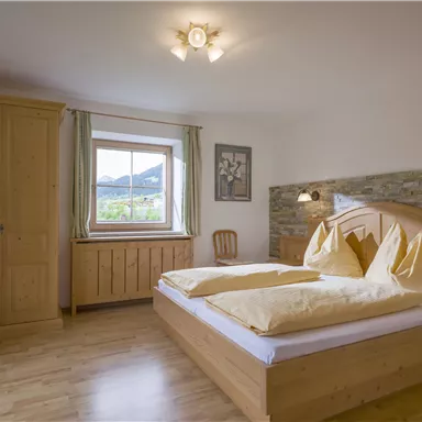 Ein gemütliches Schlafzimmer mit einem Doppelbett und zwei großen Kissen. Der Raum hat Holzmöbel und ein Fenster mit Blick auf die Landschaft.