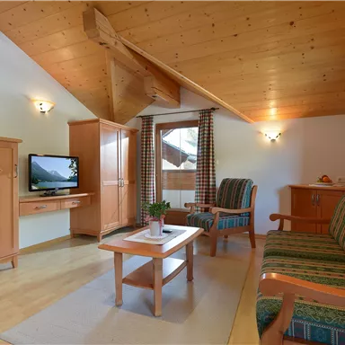 Ein gemütliches Wohnzimmer mit Holzdecken und modernen Möbeln. Es verfügt über ein Sofa, einen Couchtisch und einen Fernseher.
