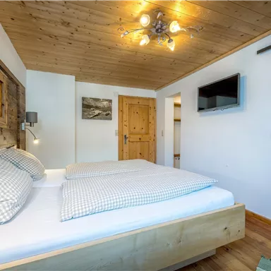 A modern bedroom with wooden walls and a cozy double bed. The amenities include a television and access to the bathroom.