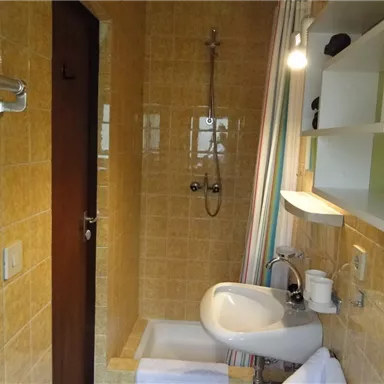 A modern bathroom with yellow tiles and a shower. There is a sink with towels and a wooden cabinet.