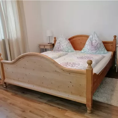 A cozy bedroom with a wooden bed and colorful pillows. Next to the bed are two nightstands with lamps.