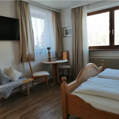 A cozy bedroom with two beds, a table, and chairs. Large windows provide plenty of daylight.