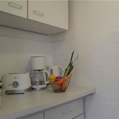 A well-equipped kitchenette with a coffee machine and a fruit basket. The walls are adorned with bright tiles.