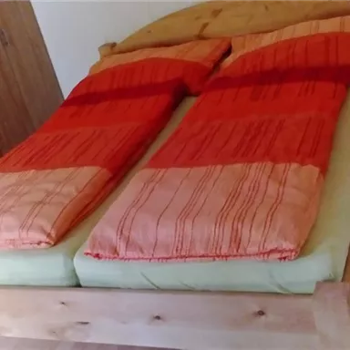 Ein Schlafzimmer mit einem Holzbett und orangefarbenen Bettdecken. Der Raum ist hell und hat einen einfachen, gemütlichen Stil.