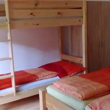 Ein gemütlicher Schlafraum mit einem Hochbett aus Holz und einem Einzelbett. Beide Betten sind mit roten und orangefarbenen Bettdecken ausgestattet.
