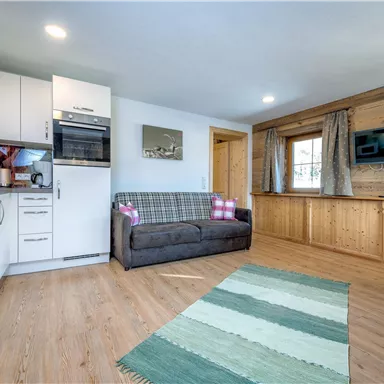 A cozy living kitchen with modern appliances and a sofa. The room has a warm wood look and is well lit.