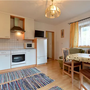 Eine helle Küche mit einem Esstisch und Stühlen. Der Raum ist gemütlich und gut ausgestattet, mit einem Teppich und großen Fenstern.