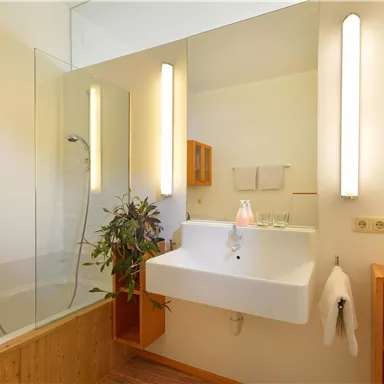 Ein modernes Badezimmer mit einer Dusche und einem eleganten Waschbecken. Die warmen Holzdetails und die Pflanzen verleihen dem Raum eine einladende Atmosphäre.