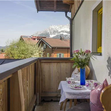 A beautiful balcony with a wooden railing and a view of the mountains. On the table, there are flowers and tea cups, perfect for relaxing.