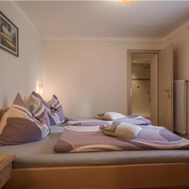 A cozy bedroom with two beds and colorful pillows. The light is soft and the walls are designed in neutral colors.