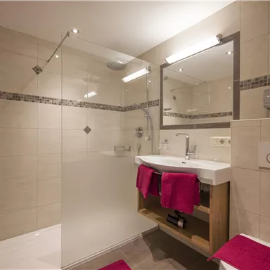 A modern bathroom with a glass shower and a sink. Pink towels and elegant tiles give the room an inviting atmosphere.