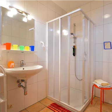 A modern bathroom with a shower cabin, a sink, and a large mirror. The walls are tiled in white, and colorful containers add a splash of color to the room.