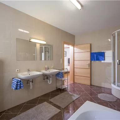 A modern bathroom with two sinks and a shower. The floor is tiled with brown tiles and there are blue towels.