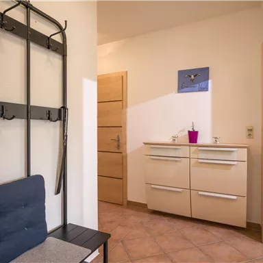 A bright hallway with a modern shoe rack and a compact washstand. The walls are kept simple and convey an inviting atmosphere.