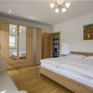 A bright bedroom with a large bed and a sofa. The room has a wardrobe and a nice wall painting.