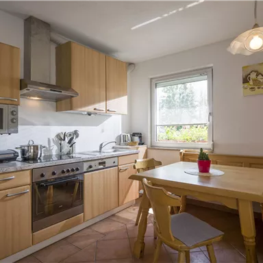A modern kitchen with wooden cabinets and a dining table. The window lets in plenty of daylight.