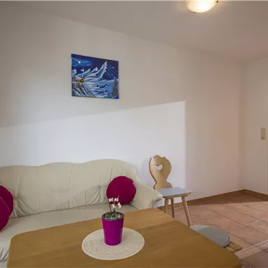 A cozy living area with a bright sofa and colorful cushions. A picture with a maritime scene hangs on the wall.