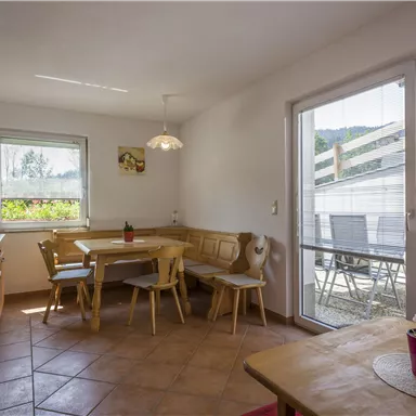 A bright kitchen with a large table and chairs. Large windows let in plenty of daylight and offer a view outside.