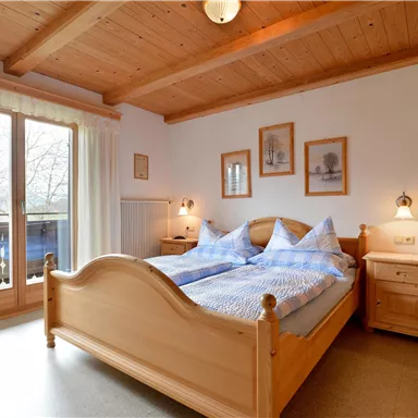 Ein gemütliches Schlafzimmer mit zwei Betten und Holzdekor. Große Fenster lassen viel Licht herein und schaffen eine einladende Atmosphäre.