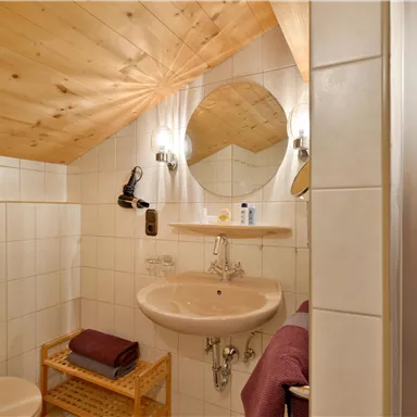 Ein modernes Badezimmer mit Holzdecke und weißen Fliesen. Es verfügt über eine Dusche, ein Waschbecken und eine helle Beleuchtung.
