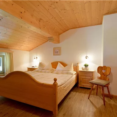 Ein gemütliches Schlafzimmer mit einem großen Bett aus Holz und warmen Holzdetails. Das Zimmer hat Fenster, die reichlich Tageslicht hereinlassen.
