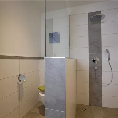 A modern bathroom with a shower and elegant tile cladding. The walls are designed in a bright and minimalist style.