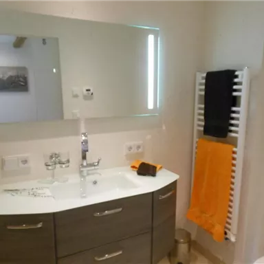 Ein modernes Badezimmer mit einem großen Spiegel und einem eleganten Waschbecken. Handtücher in kräftigen Farben hängen an einem Handtuchhalter.