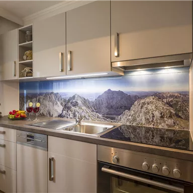 Eine moderne Küche mit hochwertigen Geräten und einem attraktiven Bergpanorama als Hintergrund. Der Raum ist hell und einladend mit frischen Früchten auf der Arbeitsplatte.