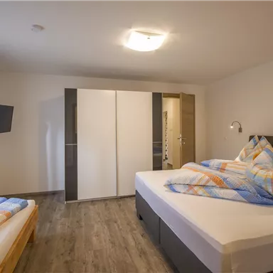 Ein modernes Schlafzimmer mit zwei Betten und einem großen Fenster. Die Wände sind hell und die Ausstattung ist minimalistisch.