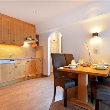 Eine moderne Küche mit Holzschränken und einem kleinen Essbereich. Der Tisch ist gedeckt und lädt zum Essen ein.