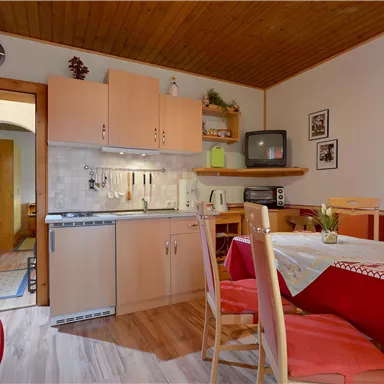 Eine gemütliche Küche mit einem Esstisch und Stühlen. Die Wände sind hell, und es gibt eine offene Verbindung zu einem anderen Raum.