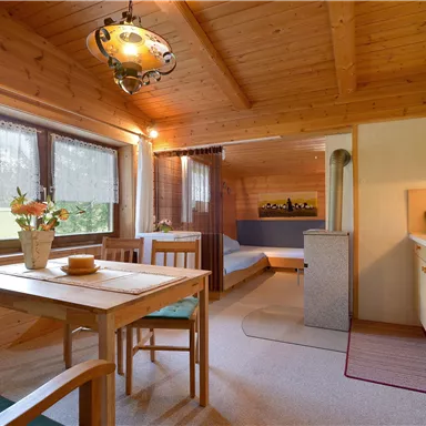 Eine gemütliche Ferienwohnung mit Holzdecken und bunten Möbeln. Der Raum umfasst eine Sitzecke, einen Essbereich und eine kleine Küche.