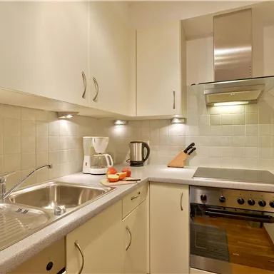 Eine moderne Küchenzeile mit hellen Schränken und Edelstahlgeräten. Auf der Arbeitsfläche stehen eine Kaffeemaschine und einige Früchte.