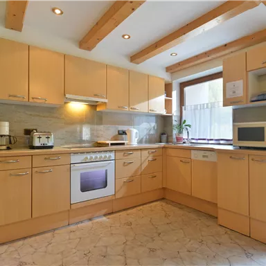 Eine moderne Küche mit Holzschränken und hellen Wänden. Im Raum sind Kühlschrank, Mikrowelle und Herd sichtbar.