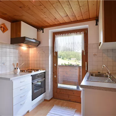 Eine helle Küche mit Holzdecken und modernen Geräten. Es gibt ein Fenster, das einen Blick ins Freie bietet.