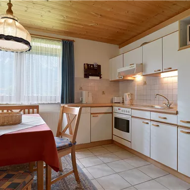 Eine moderne Küche mit einem Esstisch und Holzdekor. Sie ist hell und freundlich mit Fenstern und Elektrogeräten.