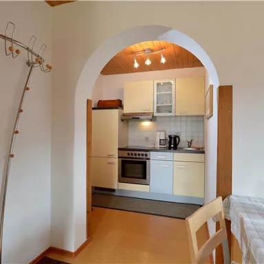 Eine helle Küche mit modernen Geräten und einem Esstisch, auf dem frisches Obst liegt. Die Umgebung ist freundlich und einladend.