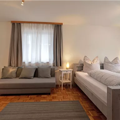 Ein helles und modernes Schlafzimmer mit einem Doppelbett und einem gemütlichen Sofa. Die großen Fenster sorgen für viel Tageslicht und eine einladende Atmosphäre.