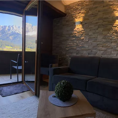 A modern living room with a view of the mountains. The space is bright and inviting, featuring a comfortable couch and a small table.