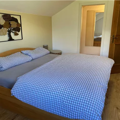 A cozy bedroom with a double bed and checked bedding. In the background, a mirror and a door are visible.