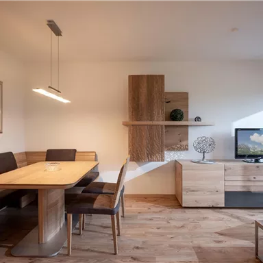 A modern living room with a large table and black chairs. On one wall there is a television and decorative elements.