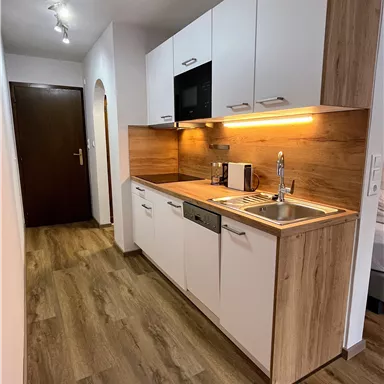 Eine moderne Küche mit weißen Schränken und Holzverkleidung. Der Boden ist aus Holz und es gibt eine angenehme Beleuchtung.