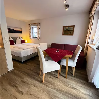 Ein gemütliches Zimmer mit zwei Betten und einem Tisch. Der Raum ist hell und einladend, mit Holzfußboden und dekorativen Fenstern.