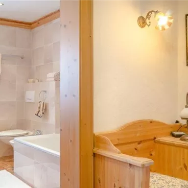 A bathroom with a bathtub and sanitary facilities that looks modern and clean. Next door is a cozy sleeping area with a wooden bed and a lamp.