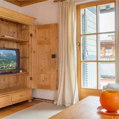 A cozy living space with a wooden TV cabinet and a window looking outside. An orange bowl sits on the table.