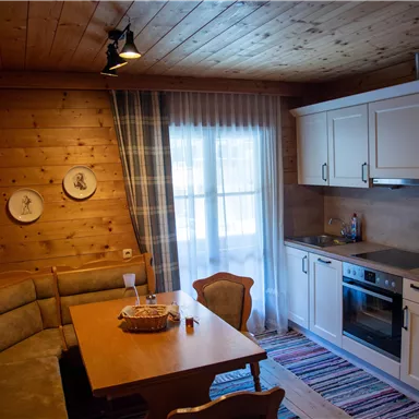 A bright and cozy kitchen with wooden paneling. A dining table with a bench, chairs, and dishes creates an inviting atmosphere.