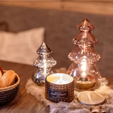 A cozy table with pastries, a scented candle, and sparkling Christmas tree decorations. The warm atmosphere invites you to relax.