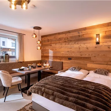 A modern bedroom with wooden walls and a cozy decor. There is a double bed, a dining area, and plenty of daylight.