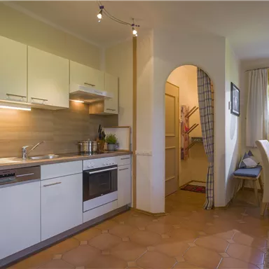 Eine moderne Küche mit weißen Schränken und einem Herd. Neben der Küche befinden sich ein Esstisch und ein gemütlicher Bereich.